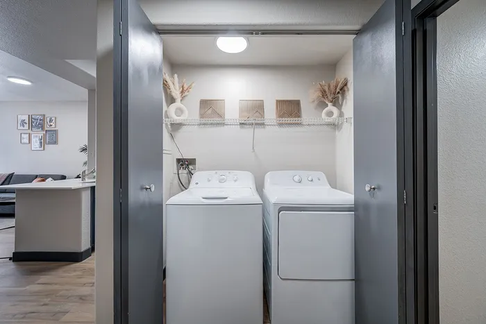 Modern laundry nook with stylish shelving and appliances, adjacent to a cozy living area in a contemporary apartment.