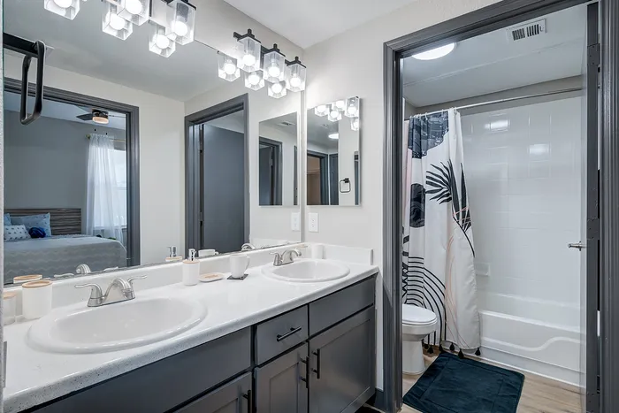 Modern bathroom with dual sinks and stylish lighting, adjacent to a cozy bedroom and sleek shower area.