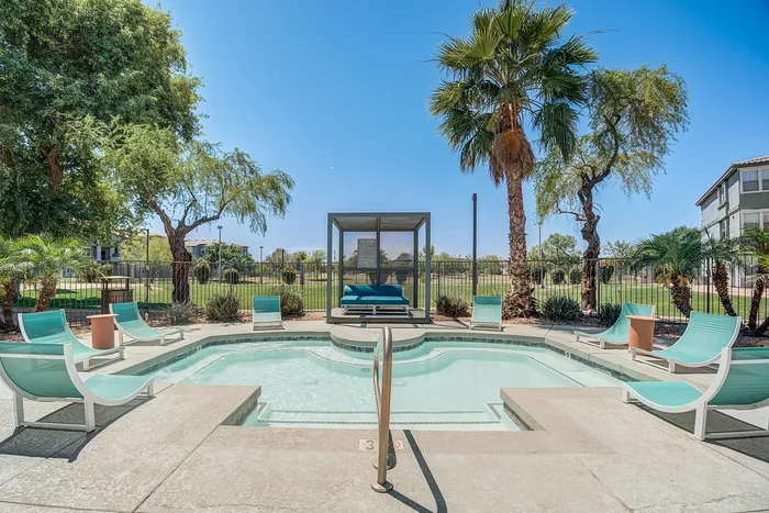 Luxurious outdoor pool area with stylish lounge chairs, tropical palm trees, and a cozy cabana set against a bright blue sky.