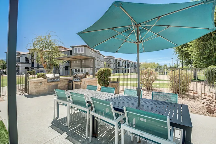 Charming outdoor patio with stylish grill area and ample seating, nestled in a modern apartment complex with scenic surroundings.