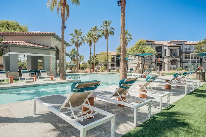 Stunning outdoor pool area with luxurious lounge chairs, surrounded by palm trees and modern apartment buildings.