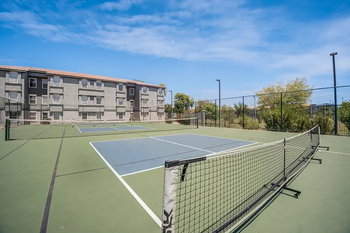 Inviting apartment complex with modern tennis courts set against a bright blue sky, ideal for an active lifestyle.