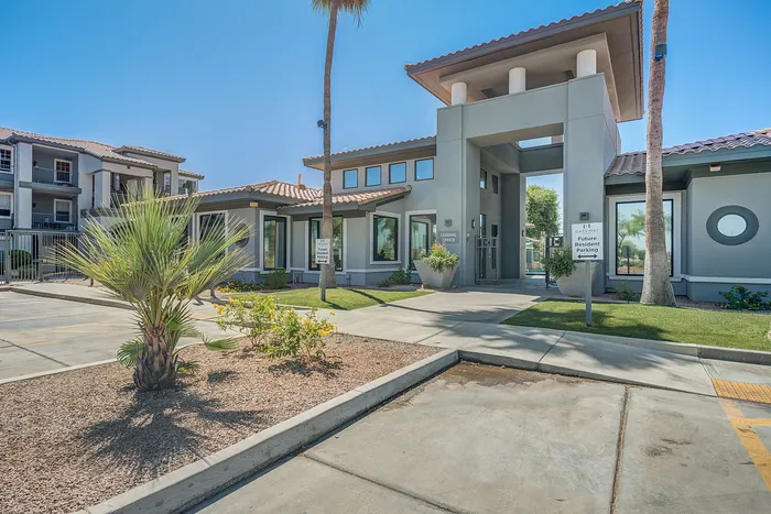 Modern apartment complex entrance with elegant landscaping and inviting architecture under a clear blue sky.