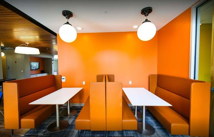 Vibrant orange-themed dining area featuring modern booth seating, sleek white tables, and stylish lighting.