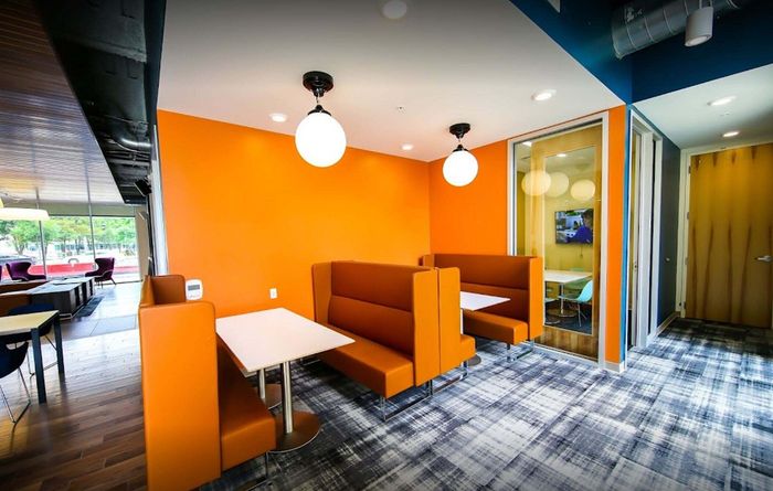 Contemporary seating area with vibrant orange booths, modern lighting, and sleek design, ideal for casual meetings and gatherings.