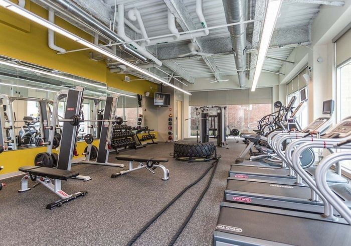 Modern gym with state-of-the-art equipment, including treadmills, weight benches, free weights, and functional training areas, set against vibrant yellow accents.