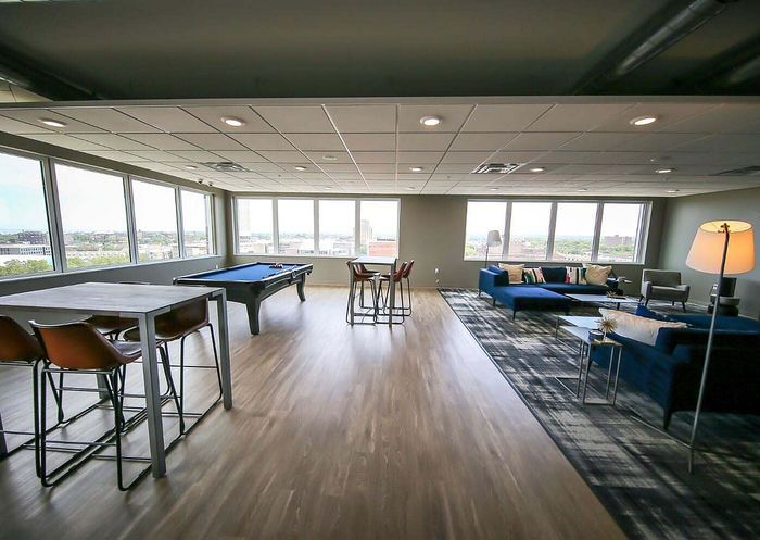 Spacious modern lounge with panoramic city views, featuring sleek wood floors, a billiards table, and stylish seating areas.