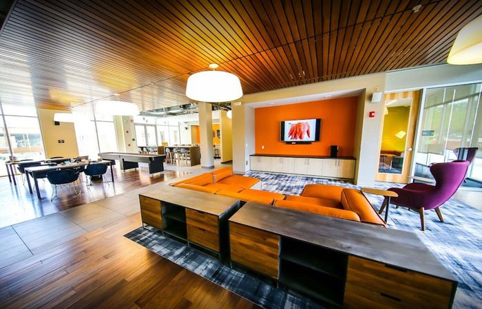 Modern and inviting communal living space with stylish orange seating, vibrant artwork, and sleek wooden finishes. Perfect for relaxation and socializing.