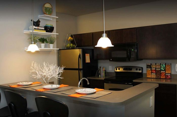 Modern kitchen with sleek dark cabinets, stainless steel appliances, and stylish breakfast bar adorned with elegant table settings and vibrant orange napkins.