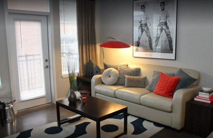 Chic urban living room with modern sofa, vibrant red and grey pillows, artistic wall decor, and stylish table lamp.