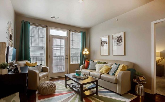Inviting living room with modern decor, featuring a cozy beige sofa, colorful cushions, and a vibrant geometric rug, illuminated by natural light through large windows.