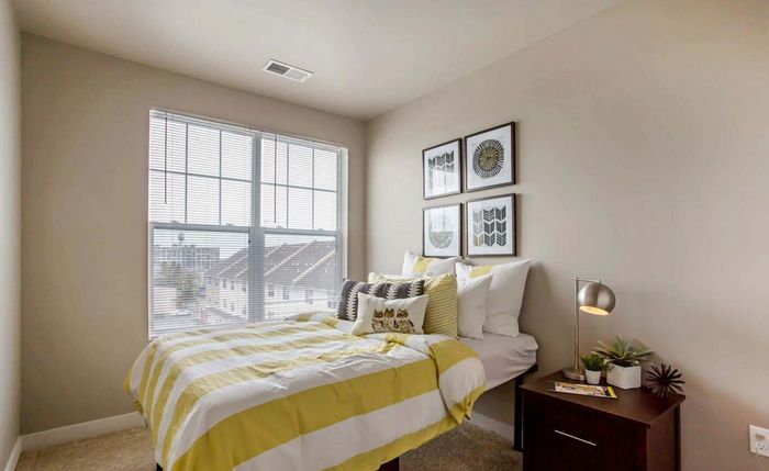 Bright and inviting bedroom with large window, cozy bed with yellow-striped duvet, stylish artwork, and modern bedside table with sleek lamp.