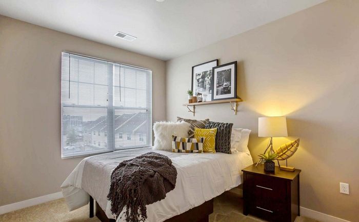Cozy bedroom featuring a sunlit window, stylish decor, and plush bedding with decorative pillows.
