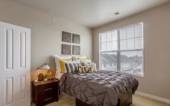 Bright and cozy bedroom with stylish decor, featuring a plush bed with decorative pillows, natural light streaming through large windows, and elegant wall art.