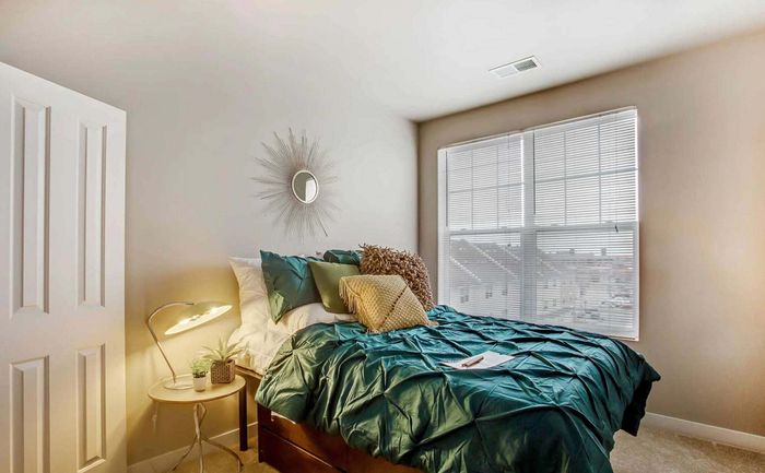 Bright and inviting bedroom with elegant sunburst mirror, luxurious teal bedding, and ample natural light from large windows.
