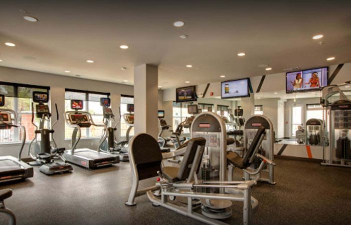 Modern fitness center with state-of-the-art exercise machines, bright lighting, and multiple TV displays.