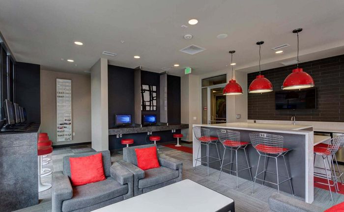 Trendy apartment lounge featuring modern seating with vibrant red accents, high-tech workstations, and a sleek bar area with industrial-style lighting.