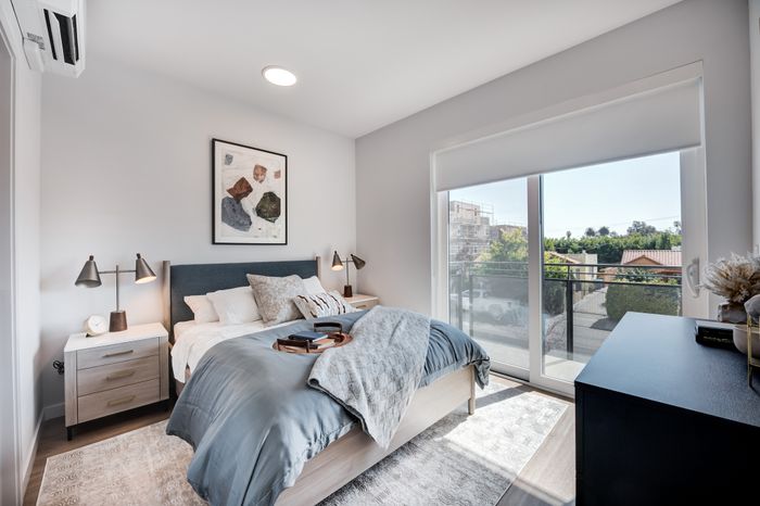 Cozy, sunlit bedroom with modern decor, stylish bed, and a balcony view offering serene greenery.