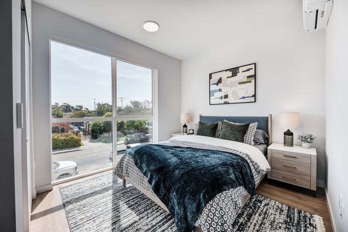 Bright and modern bedroom with a large window, plush bedding, stylish decor, and scenic city view.