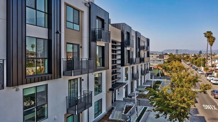 Modern apartment complex with sleek design and large windows offering cityscape views, set in a vibrant urban neighborhood.