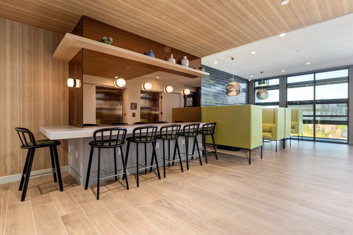 Modern community lounge with sleek bar seating and cozy green booth areas, accentuated by stylish lighting and expansive windows.