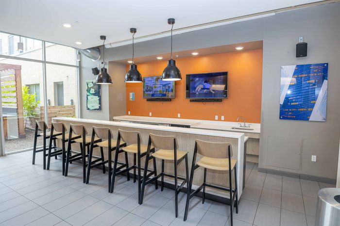 Modern communal area with sleek bar seating, pendant lighting, and dual wall-mounted TVs, perfect for social gatherings.