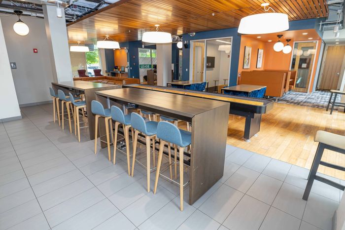 Modern communal lounge featuring sleek high tables and comfortable seating with stylish lighting and a vibrant color palette.