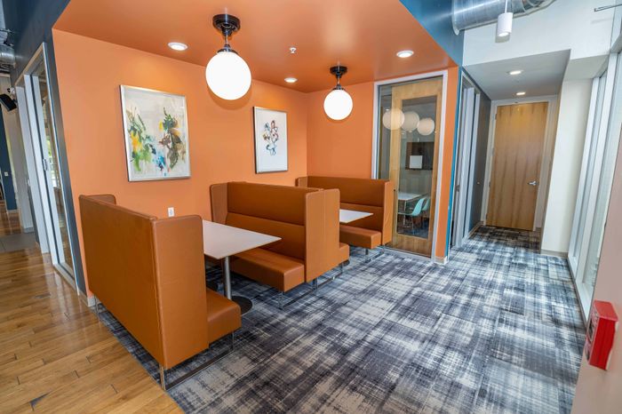 Modern communal space with cozy orange booth seating, vibrant artwork, and stylish lighting in a contemporary apartment.