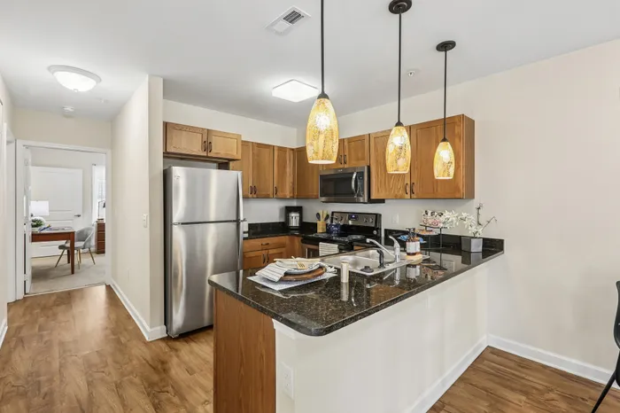 Chic kitchen featuring wood cabinetry, stainless steel appliances, and elegant pendant lighting over a polished granite island.
