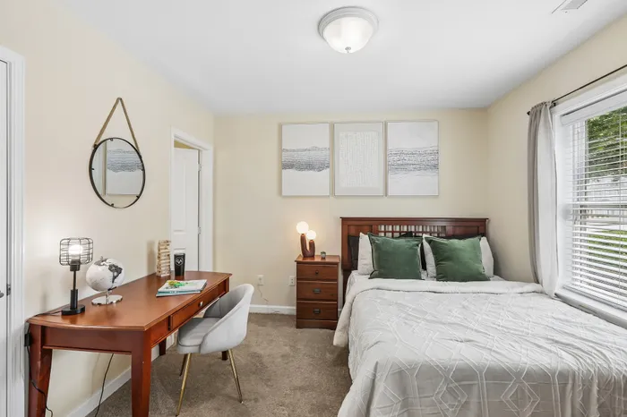 Charming bedroom with a cozy bed, stylish desk, and elegant decor, filled with natural light from large windows.