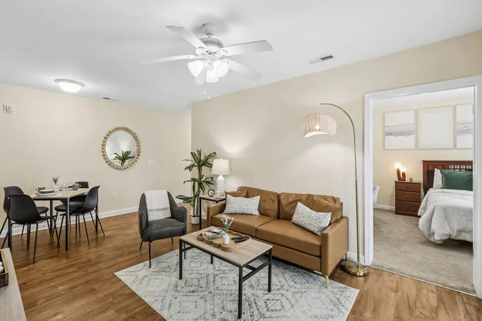 Inviting open-concept living and dining area with stylish decor, featuring a cozy brown leather sofa, elegant dining table set, and a glimpse into a chic, well-decorated bedroom.