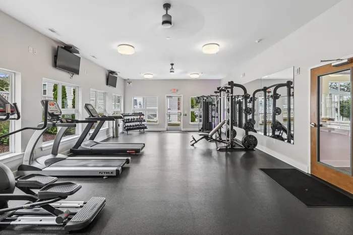 Modern, well-equipped gym with natural lighting, featuring treadmills, weight machines, and free weights.