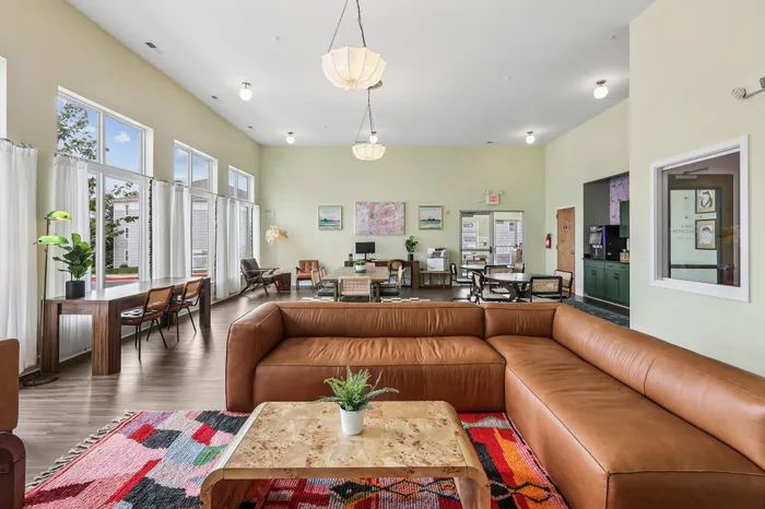Inviting communal area showcasing elegant modern decor with plush leather sofas, vibrant rug, and abundant natural light from large windows, offering a perfect blend of style and comfort.