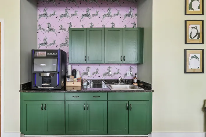Charming kitchenette with vibrant green cabinetry and playful zebra wallpaper, featuring modern coffee machine and sleek countertop.