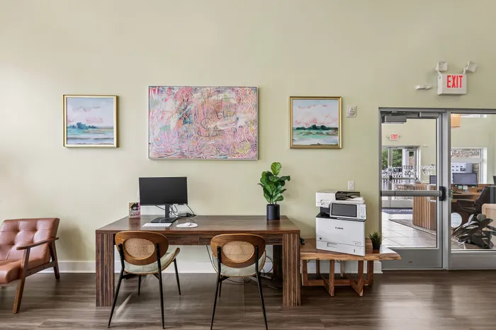 Inviting office space featuring modern wooden desk with sleek chairs, vibrant abstract and landscape art on the wall, and a glass door offering a peek into a bright interior.