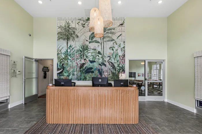 Inviting lobby space featuring a chic wooden reception desk, tropical wall art, and modern pendant lighting.