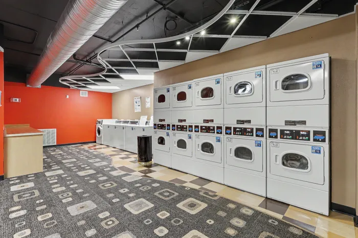 Modern apartment building laundry room with sleek washers and dryers, vibrant red accent wall, and stylish ceiling design.