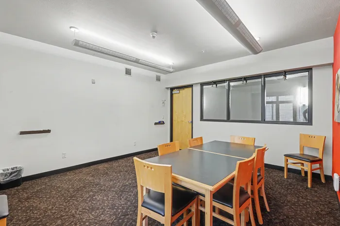Modern meeting room with stylish wooden chairs, sleek black table, and a vibrant red accent wall, offering a professional ambiance.