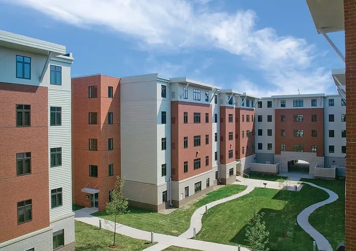 Modern apartment complex with attractive brick and siding exterior, featuring a landscaped courtyard and inviting pathways under a blue sky.