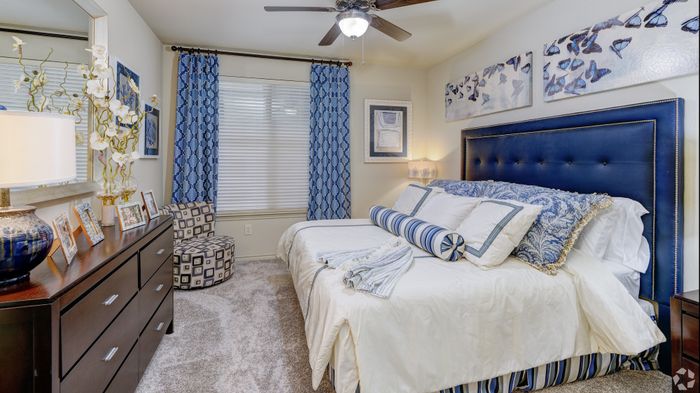 Elegant bedroom featuring a plush blue headboard, artistic butterfly decor, and rich wooden furniture. Cozy ambiance with vibrant blue curtains and tasteful floral accents.