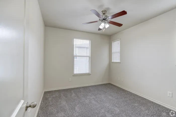 Bright and inviting bedroom with plush carpet, double windows, and modern ceiling fan.
