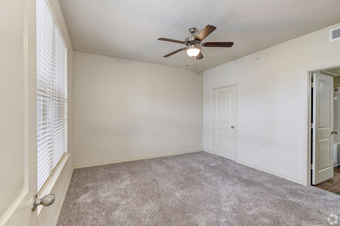 Bright and airy bedroom with plush carpet and ceiling fan, perfect for cozy living.