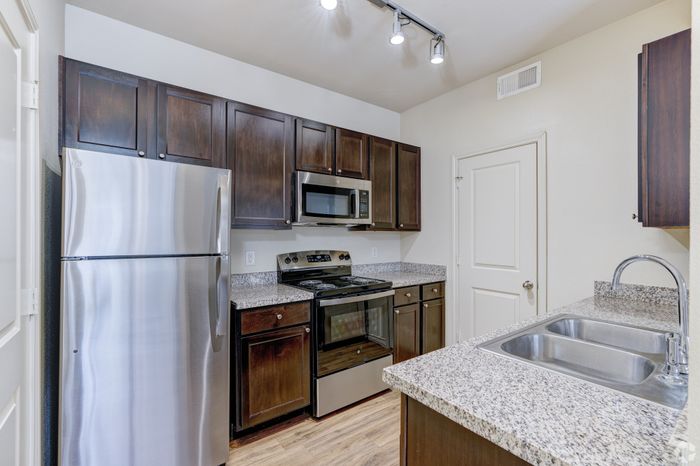 Modern kitchen featuring sleek stainless steel appliances, granite countertops, rich wood cabinetry, and ambient track lighting.