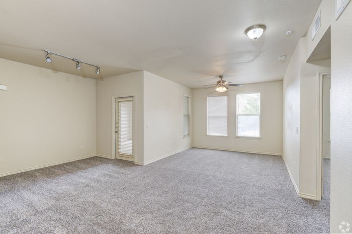 Bright and airy living room with plush carpet, ceiling fan, and ample natural light, featuring modern track lighting and a patio door.