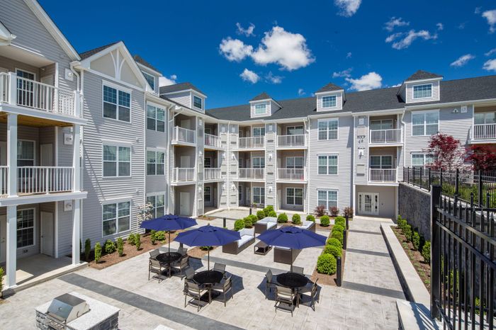 Outdoor lounge at our apartments near Tarrytown, NY, featuring outdoor couches, umbrellas, and a view of the apartments.