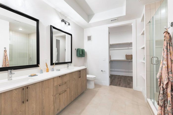 dual vanity bathroom with walk-in frameless shower and built-in linen shelves