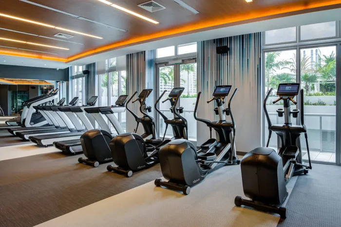 The gym at our apartments in Fort Lauderdale, featuring elliptical bikes, treadmills, and a view of the apartment complex.