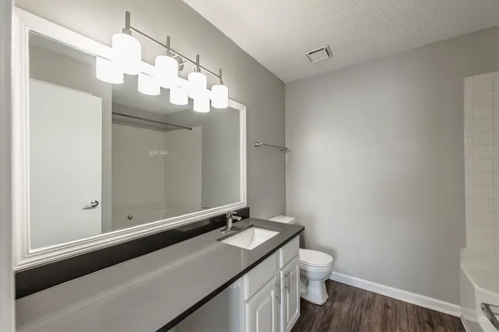 Model bathroom at our pet-friendly apartments in Nashville, TN, featuring wood grain floor paneling and grey countertops.