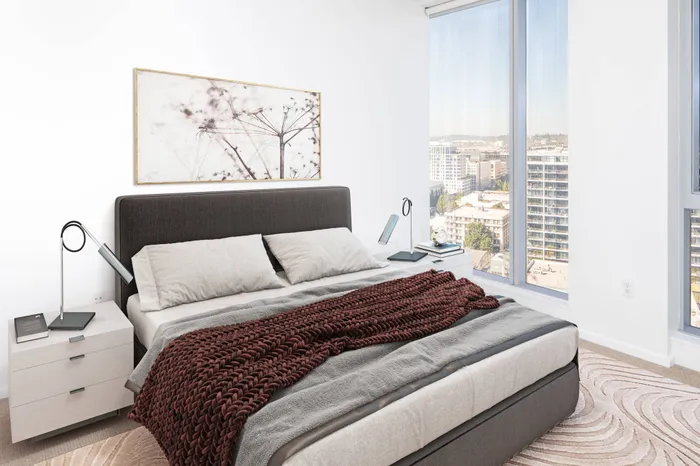 Model bedroom at our apartments in Portland, OR, featuring white and blue bedspread and floor to ceiling windows.