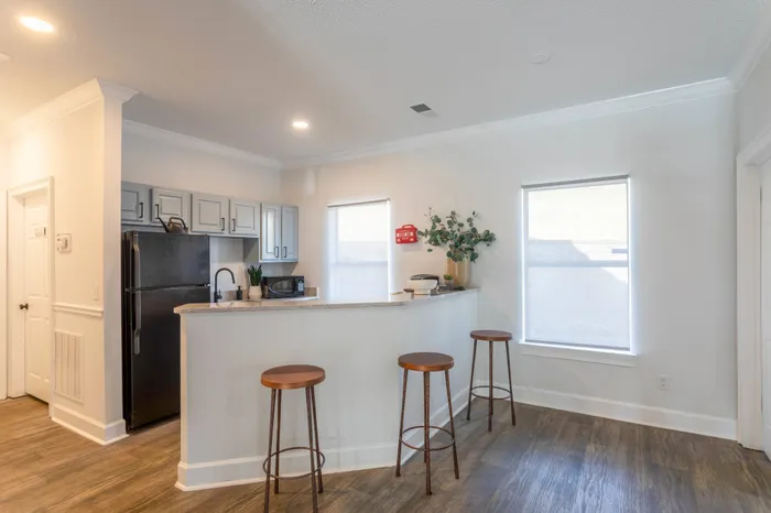 Community living room at our apartments for rent in West Nashville, featuring wood grain floor paneling and a view of the kitchen.